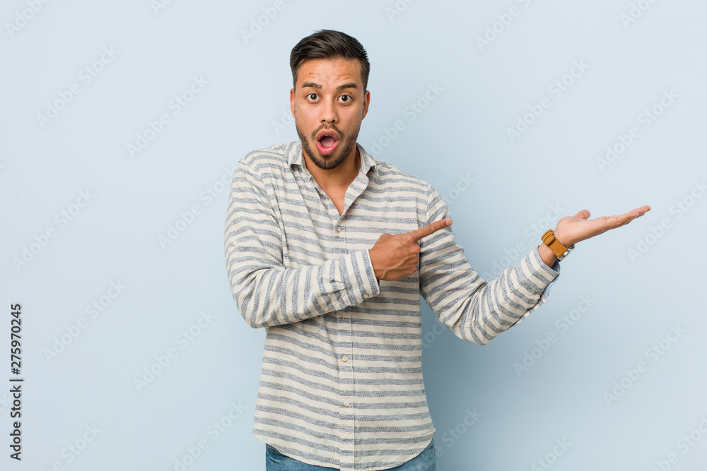 Young handsome filipino man excited holding a copy space on palm. Young handsome filipino man excited holding a copy space on palm.