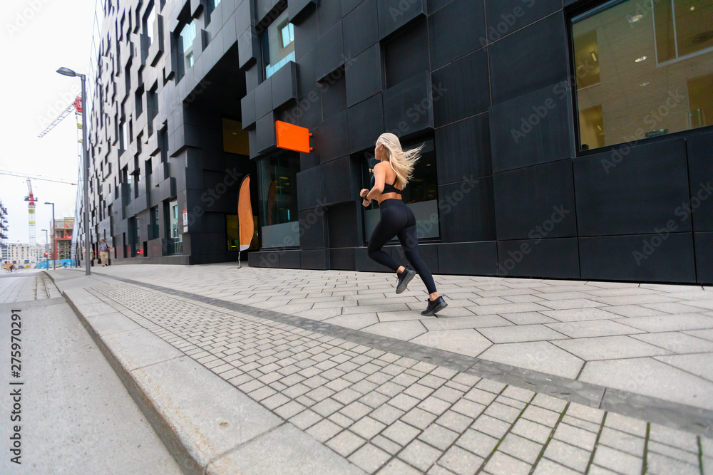 Back view of a fast running fit woman in modern city environment Back view of a fast running fit woman in modern city environment