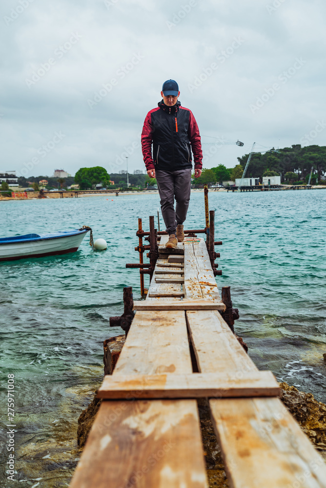 man walking by small wooden pier overcast weather stormed sea on background