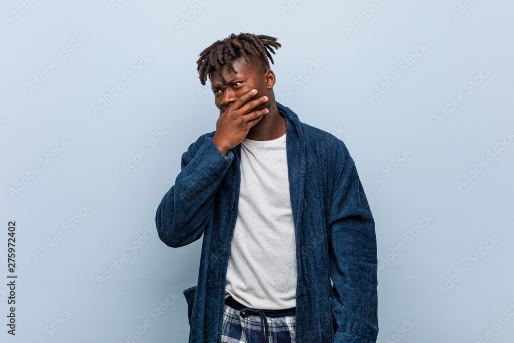 Young african black man wearing pajama thoughtful looking to a copy space covering mouth with hand. Young african black man wearing pajama thoughtful looking to a copy space covering mouth with hand.