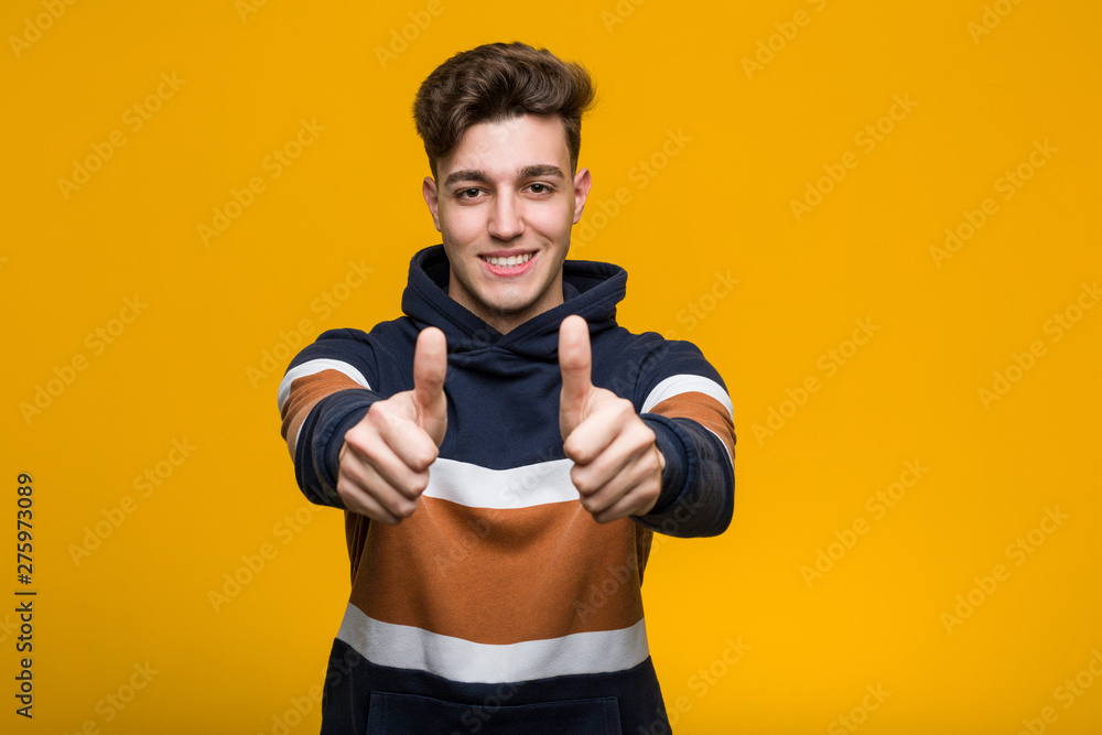 Young cool man wearing a hoodie with thumbs ups, cheers about something, support and respect concept.