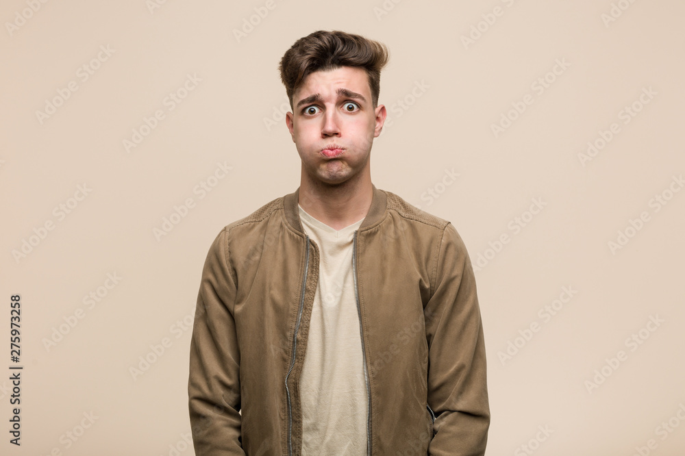 Young caucasian man wearing a brown jacket blows cheeks, has tired expression. Facial expression concept. Young caucasian man wearing a brown jacket blows cheeks, has tired expression. Facial expression concept.