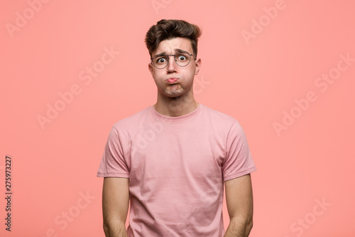 Young cool caucasian man blows cheeks, has tired expression. Facial expression concept.