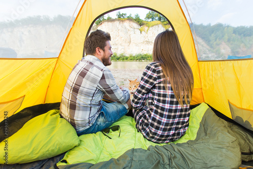 People, tourism and nature concept - Cute couple sitting with a cat in yellow tent © satura_