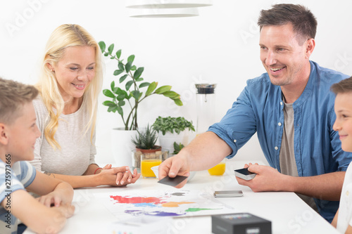 Happy young family playing card game at dining table at bright modern home. Spending quality leisure time with children and family concept. Cards are generic and debranded. photo