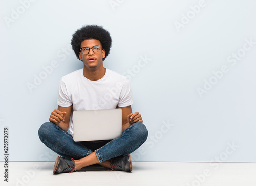 Young black man sitting on the floor with a laptop tired and bored