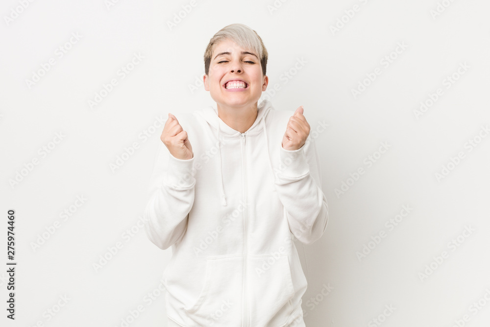 Young curvy woman wearing a white hoodie raising fist, feeling happy and successful. Victory concept. Young curvy woman wearing a white hoodie raising fist, feeling happy and successful. Victory concept.