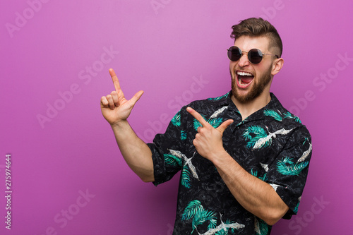 Young man wearing a vacation look pointing with forefingers to a copy space, expressing excitement and desire.
