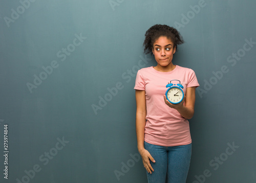 Young black woman thinking about an idea. She is holding an alarm clock. © Asier