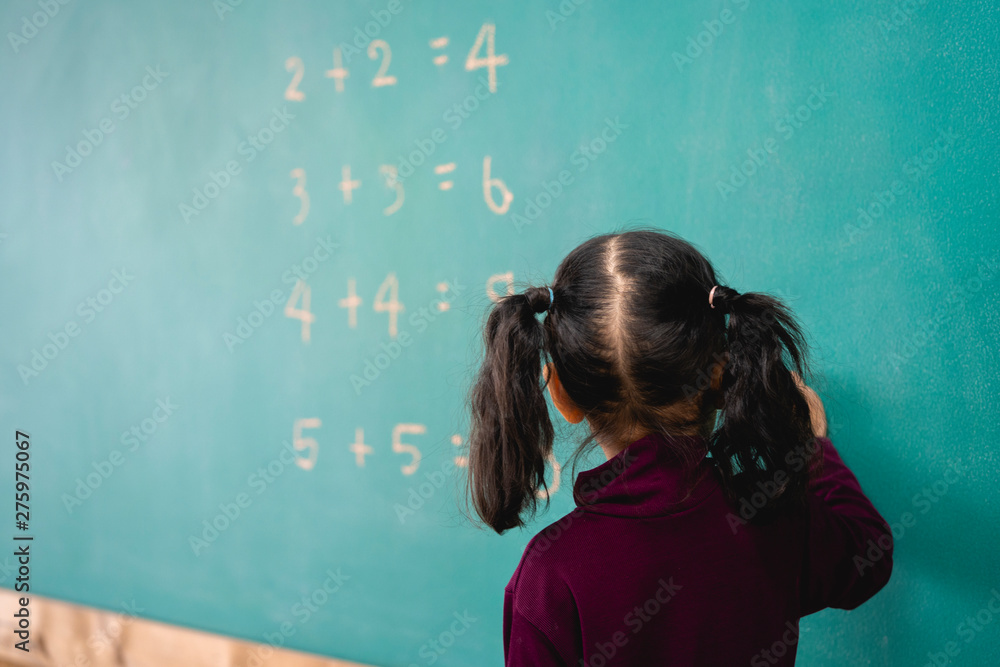 elementary school student kid writing on the green chalkboard in the classroom. Multiplication table or mathematic Education concept. elementary school student kid writing on the green chalkboard in the classroom. Multiplication table or mathematic Education concept.
