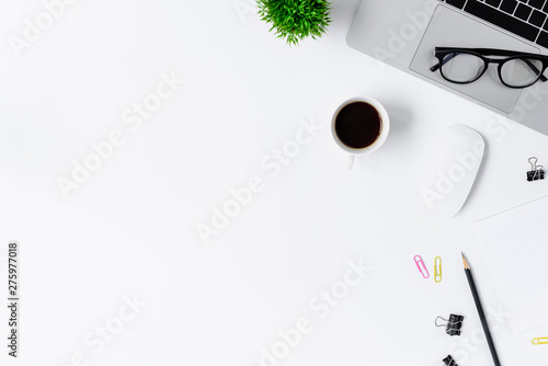 The office desk flat lay view with laptop, mouse, tree, pink and yellow paper clip, coffee cup, notebook, pencil, black glasses on white background.