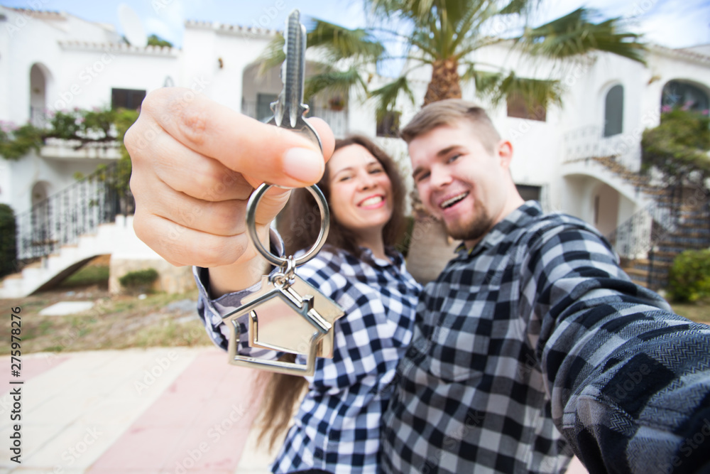 New Home, real estate and moving concept - Funny young couple showings keys from new house.
