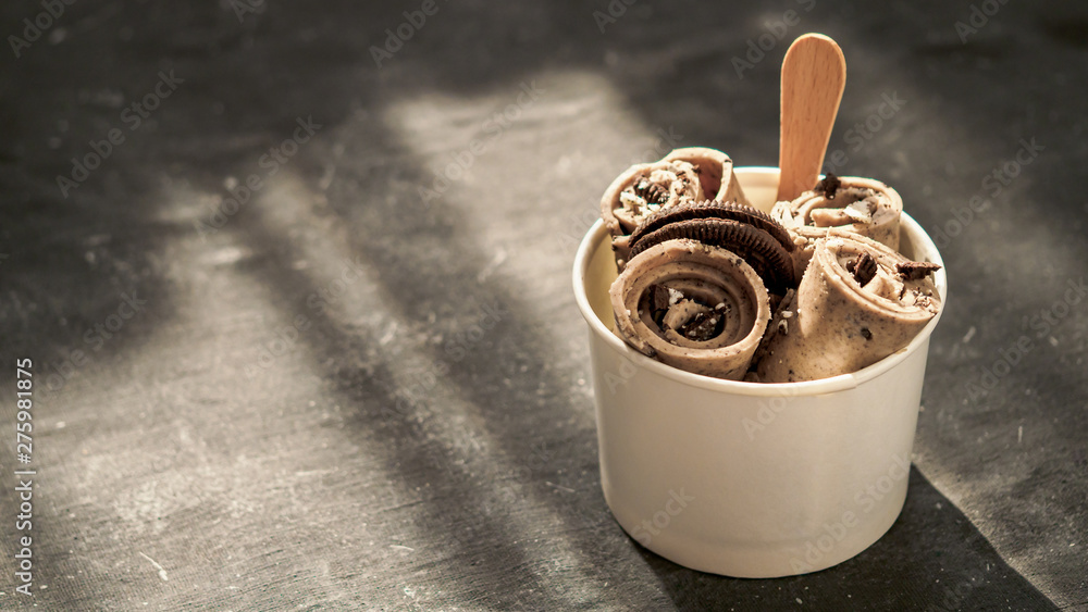 Rolled ice cream with in cone cup on dark rustic background. Iced rolls  with biscuits chocolate