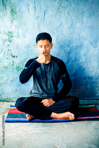 Bilde på lerret Portrait shot of the young man doing pranayama or pranayam or breath control yoga on a colorful mat with wearing black attire