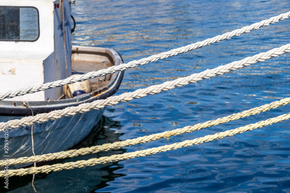 Obraz premium Four mooring lines in front of a blurred part of an old fishing boat at the Port of Kavalla, Eastern Macedonia, Northern Greece