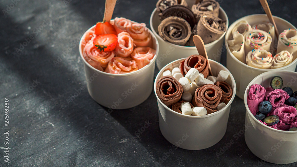Rolled ice cream in cone cups on dark background. Different iced rolls or Thai style rolled ice cream with copy space for text or design. Banner. Natural hard daylight - obrazy, fototapety, plakaty 
