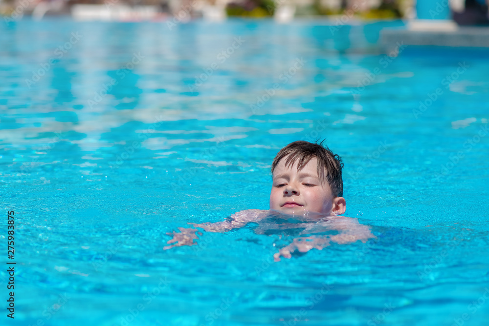 Caucasian boy spending time in pool at resort. He is learning to swim..