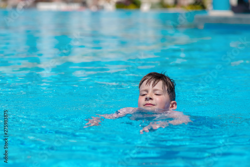 Caucasian boy spending time in pool at resort. He is learning to swim.. © Artem