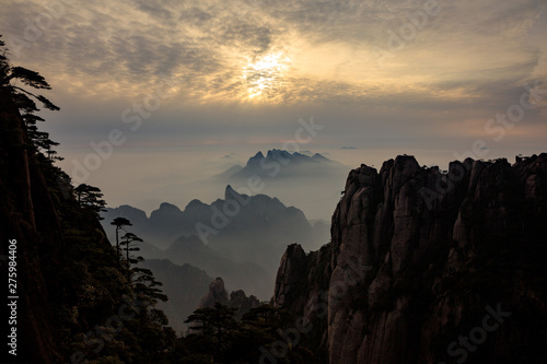 Tree silhouettes during sunset, Vibrant red and orange sky, mountains and horizon. Sanqing Mountain in Jiangxi Province, China. Mist and Fog in the distance, pine tree silhouettes.
