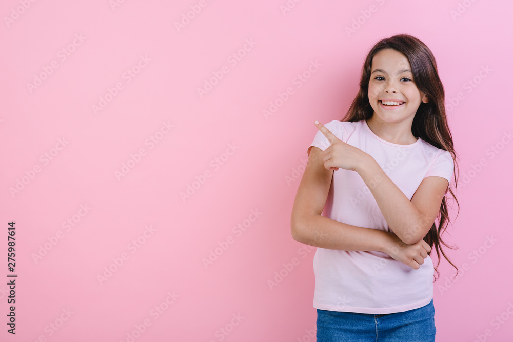 Happy young girl with folded hands stands pointing her finger in side and looking at the camera. - Image Happy young girl with folded hands stands pointing her finger in side and looking at the camera. - Image