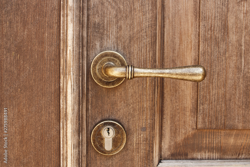 Fototapeta premium Brown wooden entrance door with bronze door handle and modern keyhole