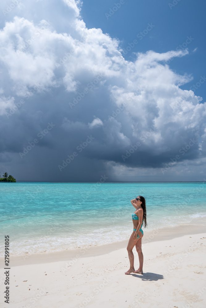 A young girl in a turquoise swimsuit is standing on a white beach.
