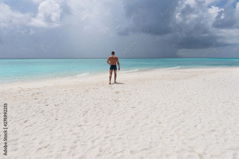 Strong young guy walking on the white sand in the turquoise water.