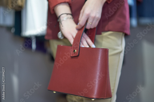 Closeup of red small bag in hand of woman. Fall spring fashion outfit red coat and trendy blue jeans