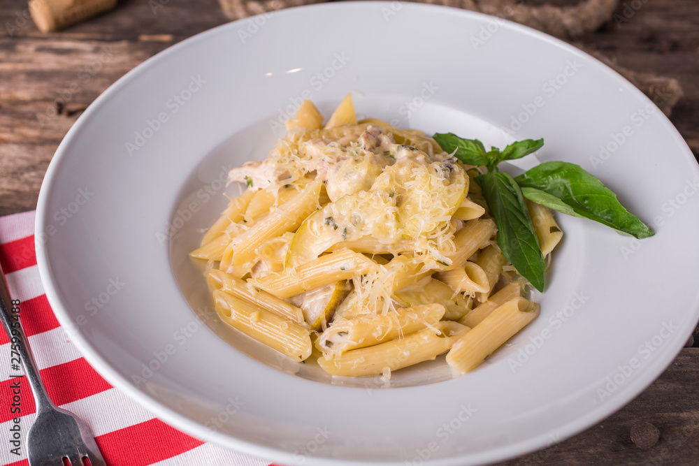 Delicious creamy Italian penne pasta starter with pepper seasoning and fresh basil on rustic wooden table