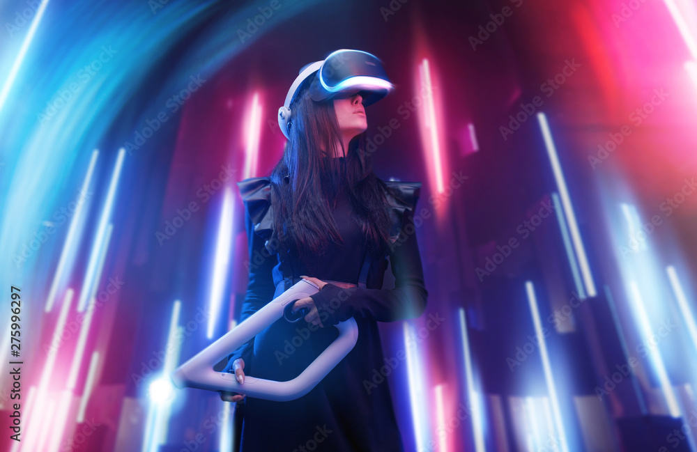 Beautiful woman in futuristic dress. Gamer girl in glasses of virtual reality with controller in hands. Augmented reality, game, future technology, hobby concept. VR. Neon light. Beautiful woman in futuristic dress. Gamer girl in glasses of virtual reality with controller in hands. Augmented reality, game, future technology, hobby concept. VR. Neon light.