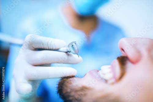 Mani di un dentista donna mentre sta per usare la fresa sui denti di un paziente uomo sulla poltrona.