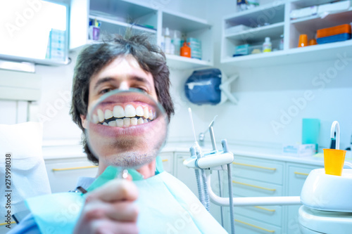 Giovane ragazzo seduto sulla poltrona del dentista, fa vedere il suo stupendo sorriso con la lente d'ingrandimento. Dopo aver fatto la pulizia dentale photo