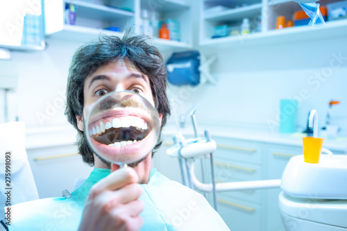 Giovane ragazzo seduto sulla poltrona del dentista, fa vedere il suo stupendo sorriso con la lente d'ingrandimento. Dopo aver tolto l'apparecchio ai denti. photo