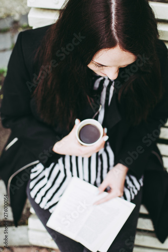 Smiling brunette girl sitting on a bench in a park and reading a soft-cover book. photo
