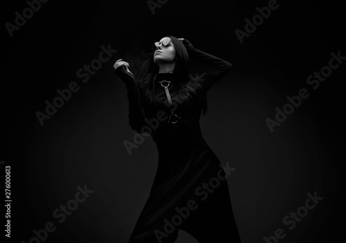 Black and white portrait of mysterious sensual beautiful brunette woman in black futuristic dress. High fashion model posing in studio on dark background.