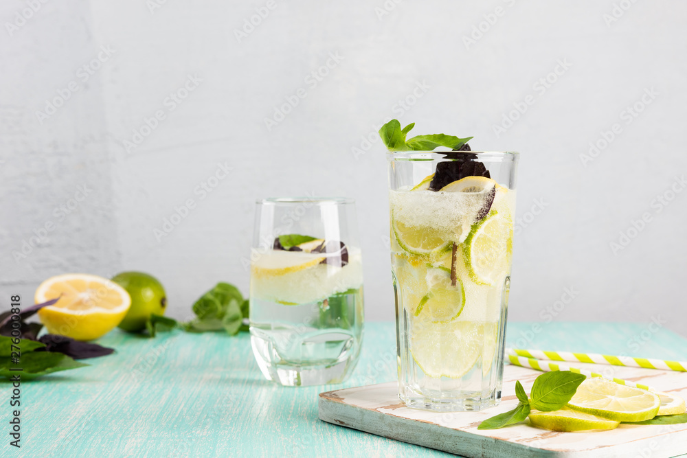 Lemonade or mojito cocktail with lemon, lime, and basil. Cold refreshing drink or beverage with ice on the wooden mint color table. Copy space for your text Lemonade or mojito cocktail with lemon, lime, and basil. Cold refreshing drink or beverage with ice on the wooden mint color table. Copy space for your text