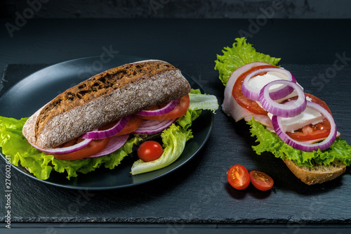 Breakfast tomato sandwich with salad on black stone background.