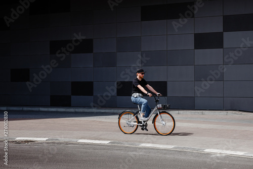 Stylish guy dressed in trendy jeans clothes rides bicycle in the street against the background of a gray building