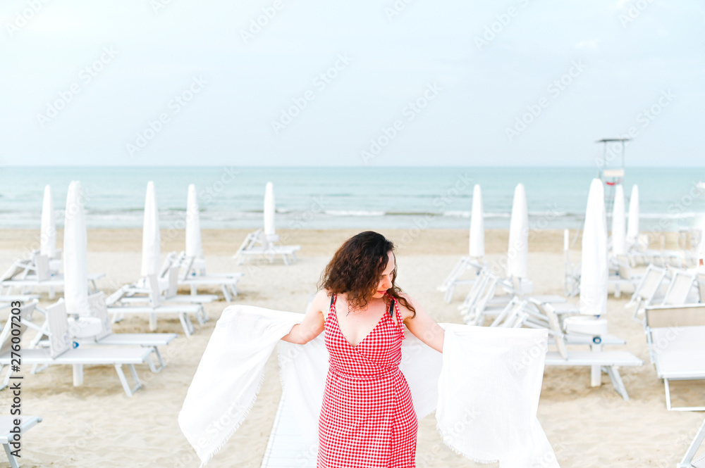 Obraz premium A woman in a red dress and curly hair is standing on the beach. A man with happy emotions. Walk along the sea promenade. Travel and tourism in the summer. Copy space