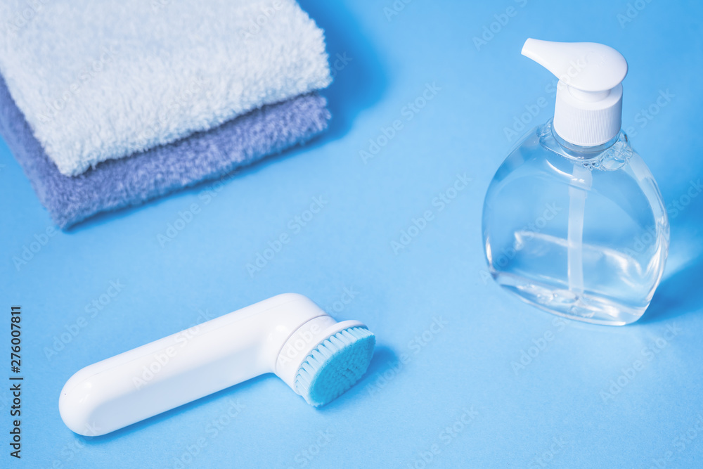 Liquid transparent soap bottle, facial pore cleansing brush and two towels on blue background with toothbrush. Hygien purity beauty care and bathroom spa with copy space Liquid transparent soap bottle, facial pore cleansing brush and two towels on blue background with toothbrush. Hygien purity beauty care and bathroom spa with copy space