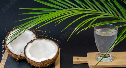 Exotic fruit Coconut, two halves of fruit in the shell, dark background, a glass of coconut water on the kitchen and blackboard, green palm trees, selective focus