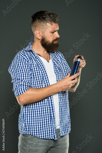 The best shampoo for his hair. Bearded man holding shampoo bottle on grey background. Hipster with beard and mustache choosing shampoo for cleaning hair. Daily strengthening shampoo for men photo