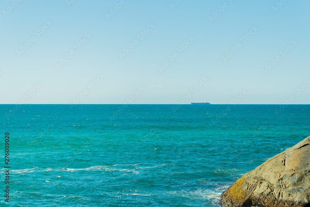 Vista de um grande navio navegando no horizonte do oceano Atlântico e uma encosta.