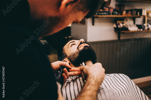 Hair beard and mustache treatment in barber shop. Young, bearded, muscular, handsome barber making haircut of attractive bearded man in barbershop