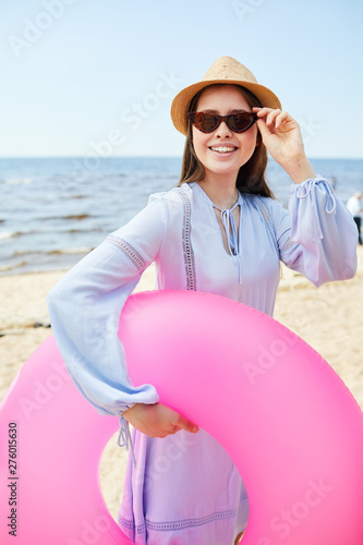 Waist up portrait of happy young woman posing with pink swim tube at beach enjoying Summer, copy pace photo