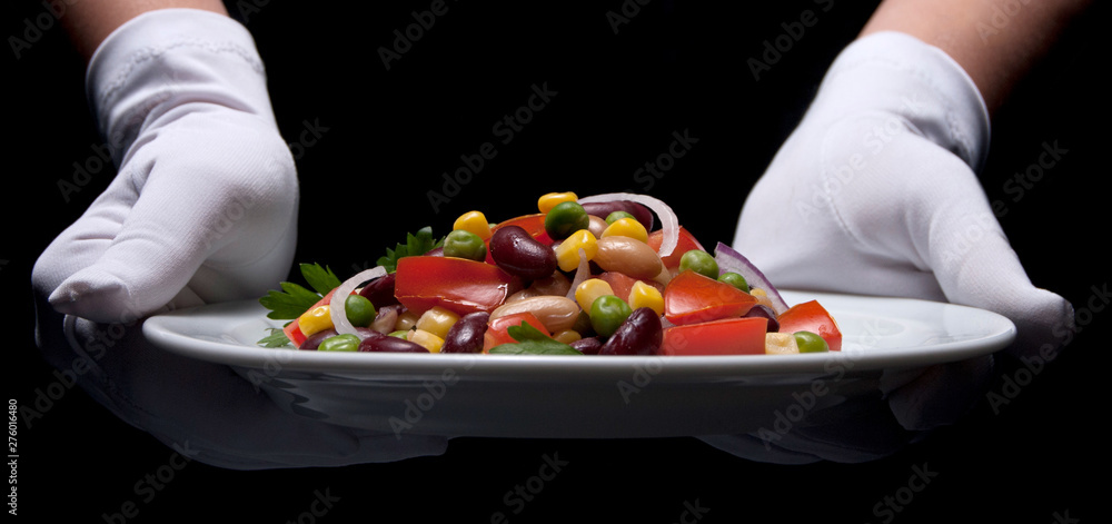 Healthy bean and corn salad on a white plate served by someone in white gloves Healthy bean and corn salad on a white plate served by someone in white gloves