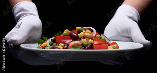 Healthy bean and corn salad on a white plate served by someone in white gloves