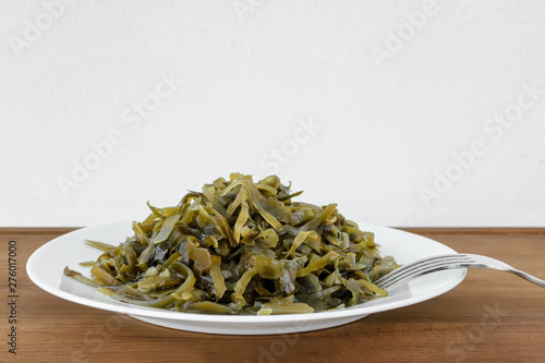 Pickled kelp slices and a fork on a plate over brown wooden table. Edible seaweed contains a lot of iodine and microelements. Seafood  vegetarian nutrition and healthy eating.