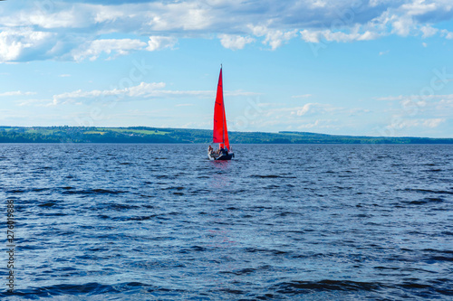 sailboat with scarlet sails in the middle of a wide lake