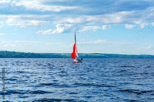 sailboat with scarlet sails makes a turn maneuver against the backdrop of a wooded shore